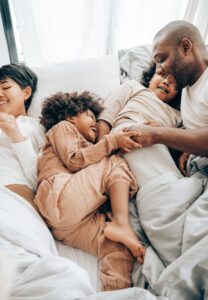 family smiling and cuddling in bed after lytle dental cleanings